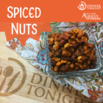 A bowl of our Spiced Nut recipe ready for your next party on a festive table cloth and a wooden cutting board!