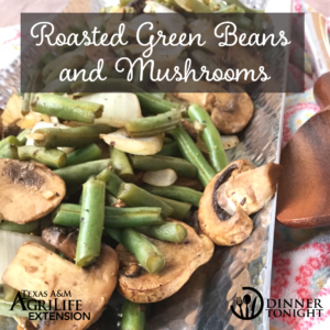Roasted Green Beans and Mushrooms recipe plated in a silver serving dish with wooden serving spoons.