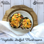 Stuffed Portabella Mushroom recipe from Dinner Tonight, two mushrooms on a white plate, stuffed with veggies and cheddar cheese.
