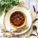 Slow cooker Taco Soup recipe ready to warm you up! plated in a bowl surrounded by chilis and cilantro.
