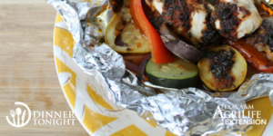 Chicken and vegetables still in their grilling packet, on a yellow plate ready to be served.